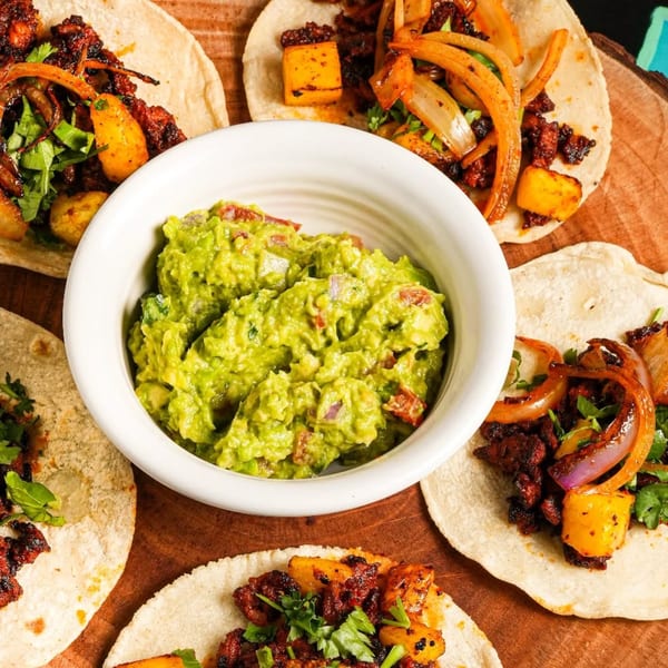 Five La Fiesta Mexican Cocina tacos with meat, pineapple, onions, cilantro, and a bowl of guacamole.