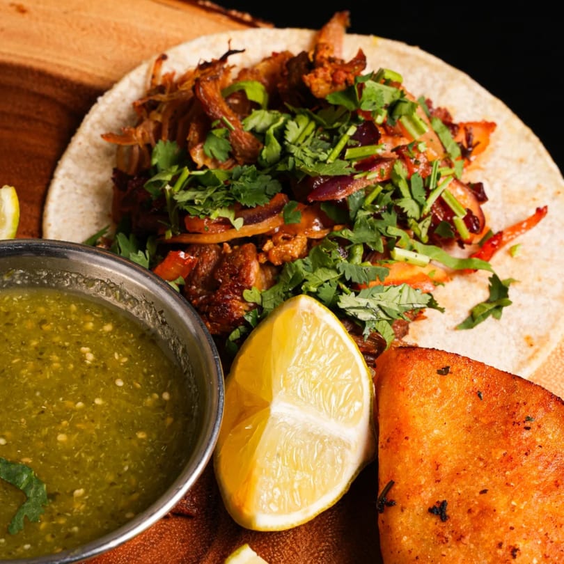 A La Fiesta Mexican Cocina taco with meat, cilantro, and onions, served with salsa verde and lime.