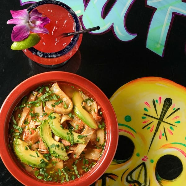 Mexican tortilla soup with avocado, a red drink with a purple orchid, and a yellow sugar skull.