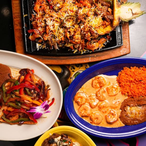 A vibrant spread of Mexican dishes, including fajitas, shrimp in sauce, and rice, on a colorful table.