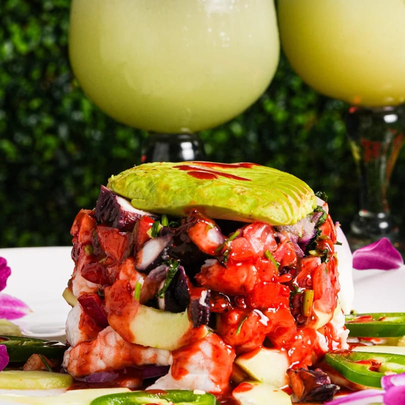 Mexican seafood ceviche with octopus, shrimp, avocado, and red sauce, garnished with jalapeños.