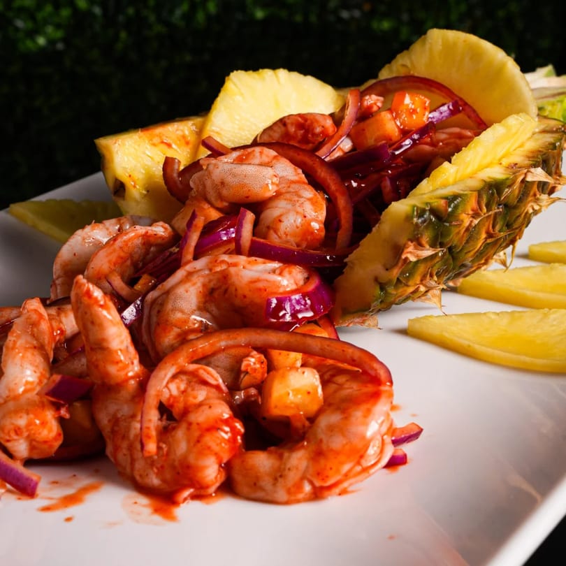 Mexican shrimp dish with red sauce, red onions, and pineapple slices on a white plate.